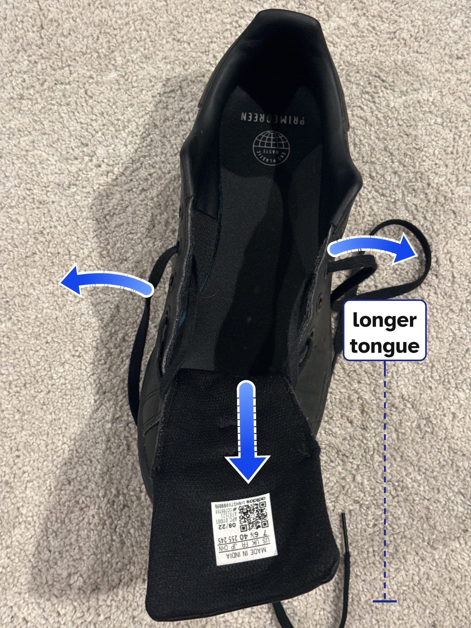 A black sneaker seen from above, its laces loosened and its sides spreading outward, its long tongue folded down toward the toe and marked “longer tongue.”