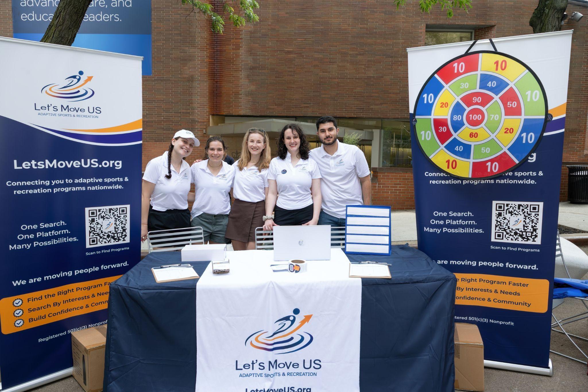 The five Let's Move US volunteers standing behind their booth table, flanked by Let's Move US banners.
